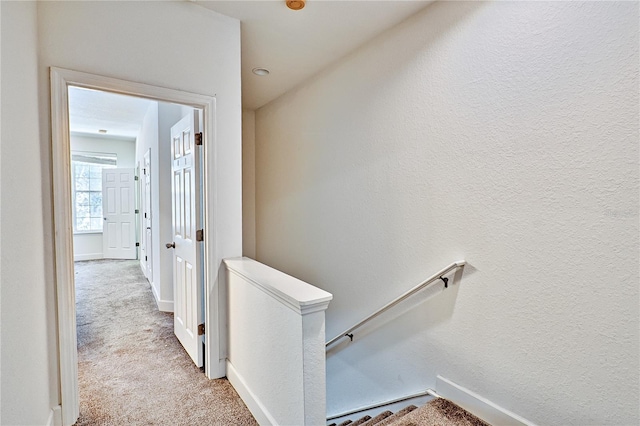 corridor featuring an upstairs landing, baseboards, carpet, and a textured wall