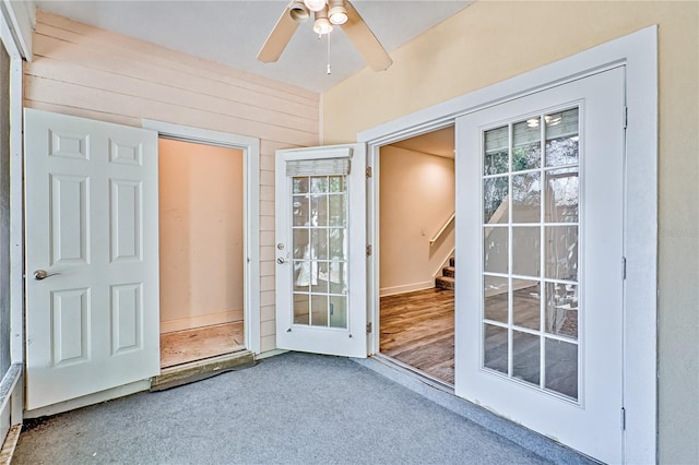 doorway with wooden walls, stairway, carpet, and ceiling fan