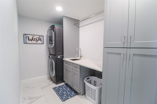 clothes washing area with baseboards, cabinet space, marble finish floor, stacked washer / drying machine, and a sink