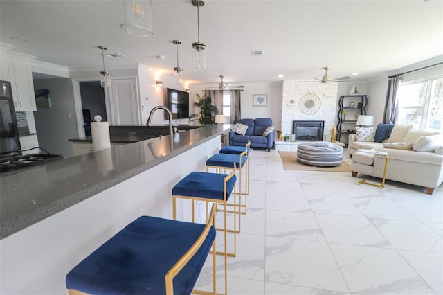 kitchen with a breakfast bar area, a fireplace, crown molding, decorative light fixtures, and marble finish floor