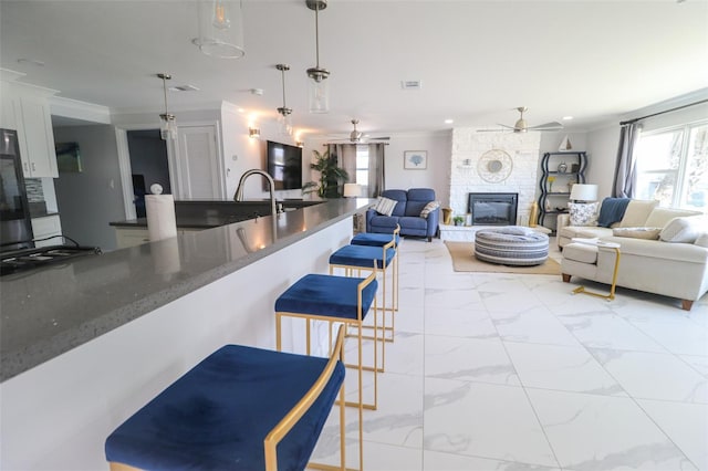 817 Blue Heron Blvd, Ruskin, FL 33570 - kitchen featuring a ceiling fan, light marble finish flooring, a fireplace, ornamental molding, and a breakfast bar area