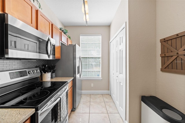 kitchen featuring light tile patterned floors, baseboards, stainless steel appliances, brown cabinets, and backsplash