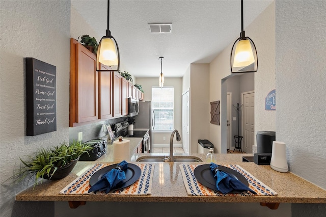 kitchen featuring visible vents, appliances with stainless steel finishes, a textured wall, brown cabinetry, and a sink