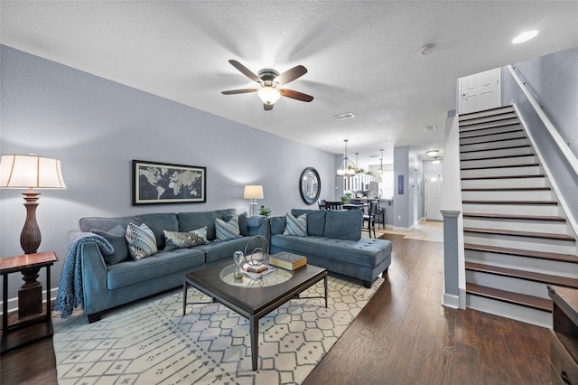 living area featuring stairway, ceiling fan with notable chandelier, a textured ceiling, and wood finished floors