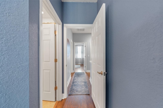 corridor featuring visible vents, baseboards, wood finished floors, and a textured wall