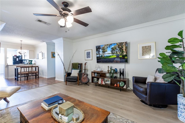 living area with visible vents, ceiling fan with notable chandelier, a textured ceiling, wood finished floors, and crown molding