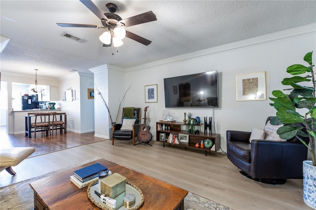 living room featuring visible vents, crown molding, ceiling fan with notable chandelier, wood finished floors, and a textured ceiling