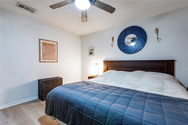 bedroom featuring visible vents, a textured ceiling, wood finished floors, baseboards, and ceiling fan