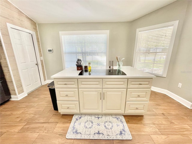 kitchen with a center island with sink, light wood-style floors, light countertops, black electric cooktop, and baseboards