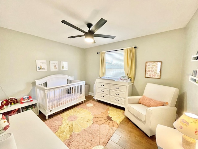 bedroom with a crib, a ceiling fan, and wood finished floors