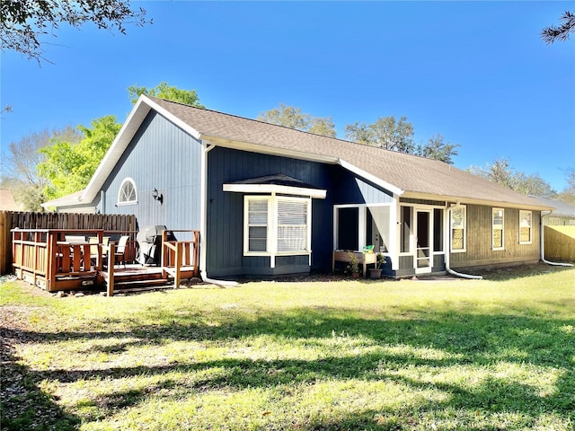 rear view of property with a deck, fence, a lawn, and a shingled roof