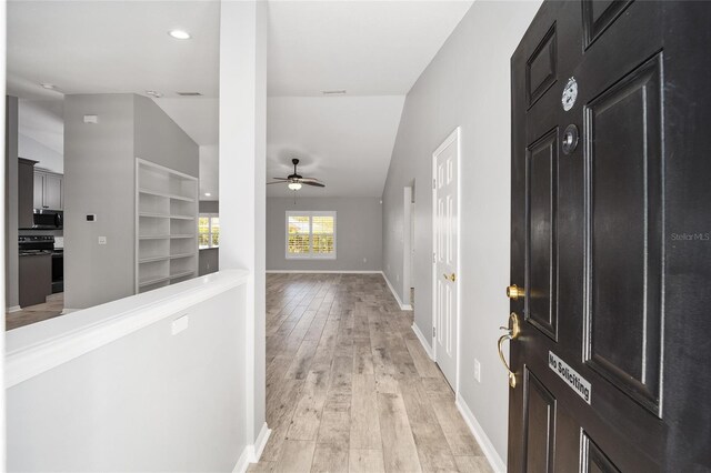 corridor featuring vaulted ceiling, baseboards, and light wood finished floors