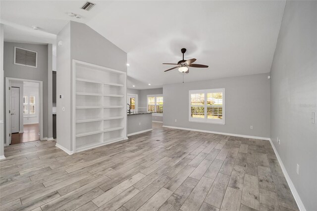 unfurnished living room featuring visible vents, light wood-style flooring, baseboards, and lofted ceiling