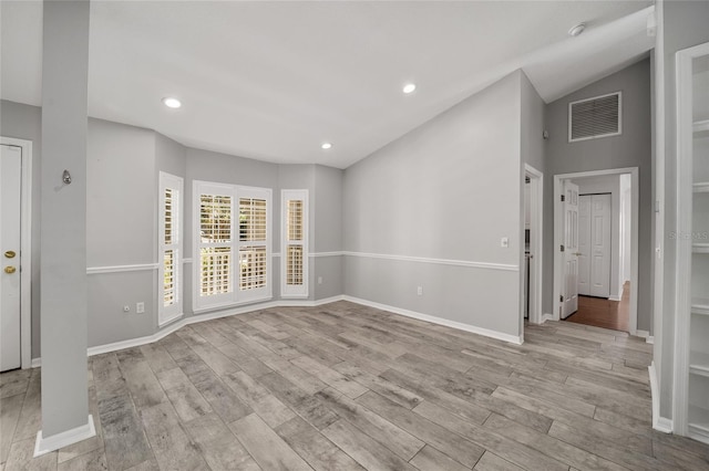 spare room with visible vents, baseboards, vaulted ceiling, and light wood finished floors