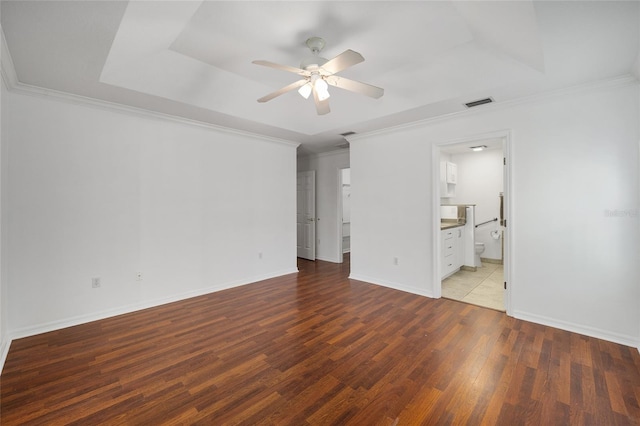 unfurnished bedroom featuring wood finished floors, visible vents, baseboards, crown molding, and a raised ceiling