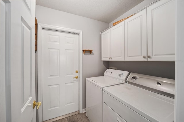 laundry area with cabinet space, separate washer and dryer, light wood-type flooring, and a textured ceiling