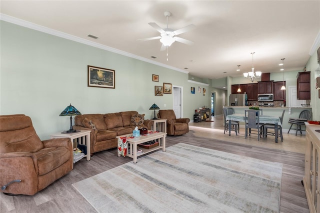 living area featuring visible vents, ceiling fan with notable chandelier, ornamental molding, and light wood finished floors