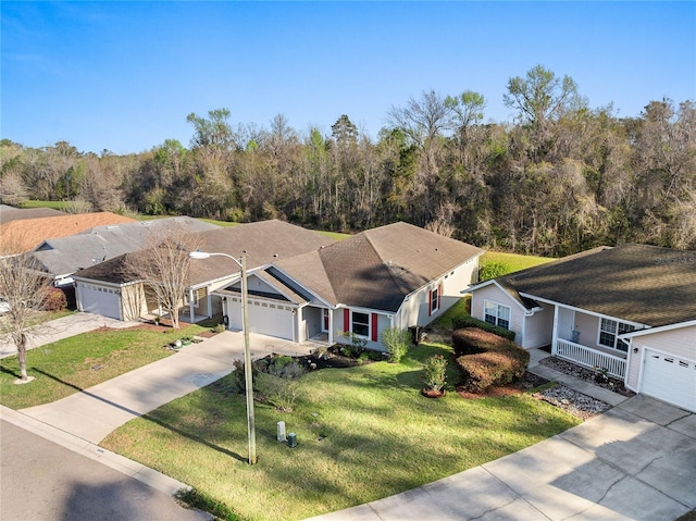 view of front of house featuring a porch, concrete driveway, a front yard, a view of trees, and an attached garage