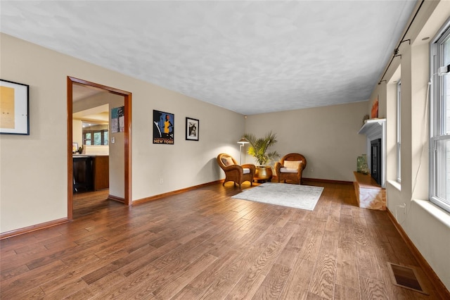 sitting room with visible vents, a fireplace with raised hearth, baseboards, and wood finished floors