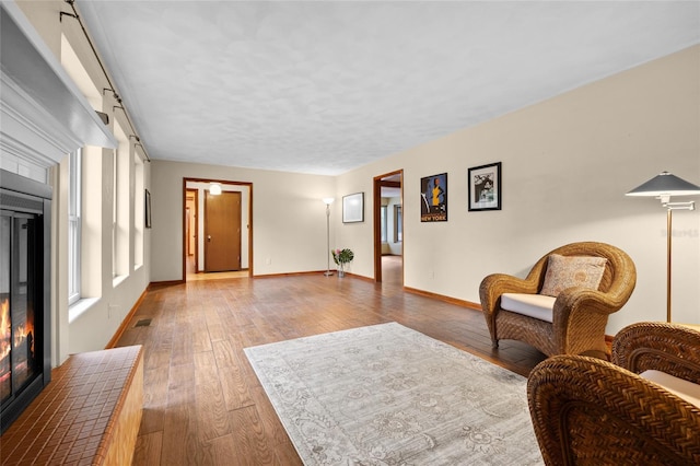 sitting room with visible vents, a textured ceiling, a glass covered fireplace, hardwood / wood-style floors, and baseboards