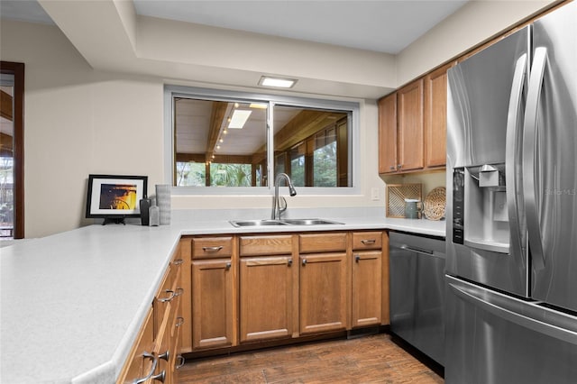 kitchen with brown cabinetry, dark wood finished floors, a sink, light countertops, and appliances with stainless steel finishes