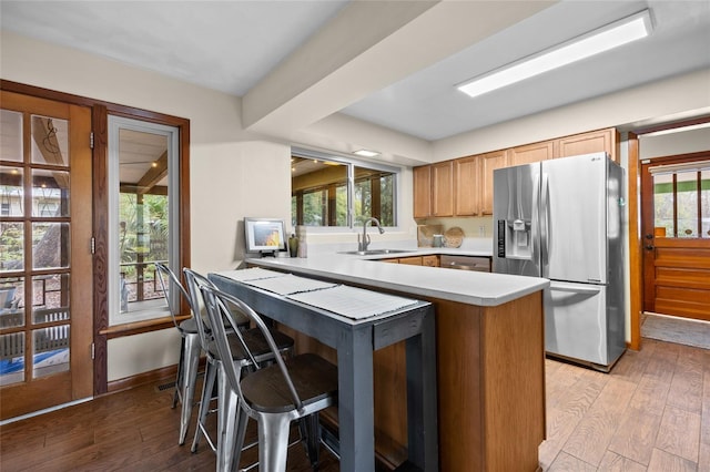 kitchen with stainless steel fridge, a peninsula, light wood-style flooring, and a sink