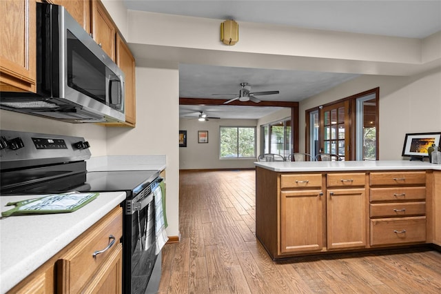 kitchen with light wood-type flooring, stainless steel appliances, light countertops, open floor plan, and brown cabinets