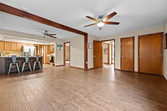 unfurnished living room with a ceiling fan, beam ceiling, wood finished floors, and baseboards