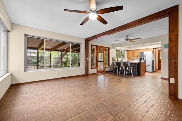 unfurnished living room with baseboards, beam ceiling, ceiling fan, and light wood finished floors