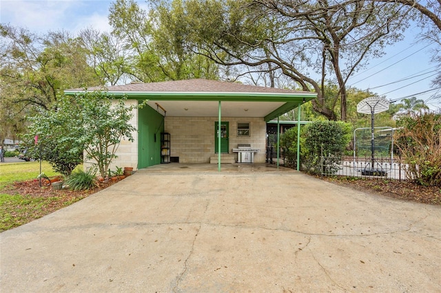 exterior space featuring concrete block siding, fence, driveway, and a carport