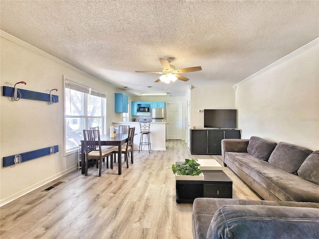 living room featuring ornamental molding, visible vents, light wood finished floors, and ceiling fan