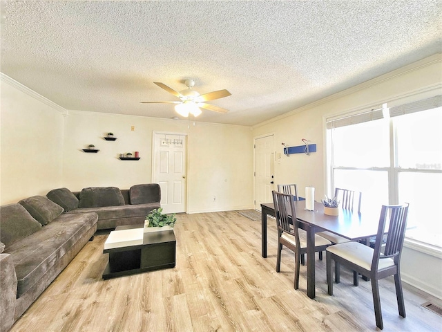 living area featuring visible vents, light wood-style floors, a ceiling fan, and crown molding