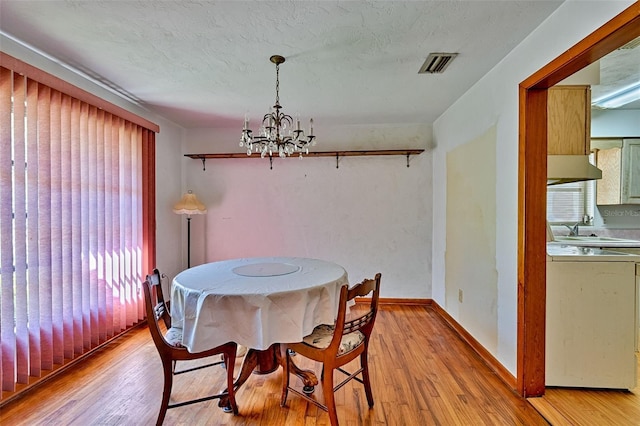 dining space with light wood-style flooring, a notable chandelier, visible vents, and a textured ceiling