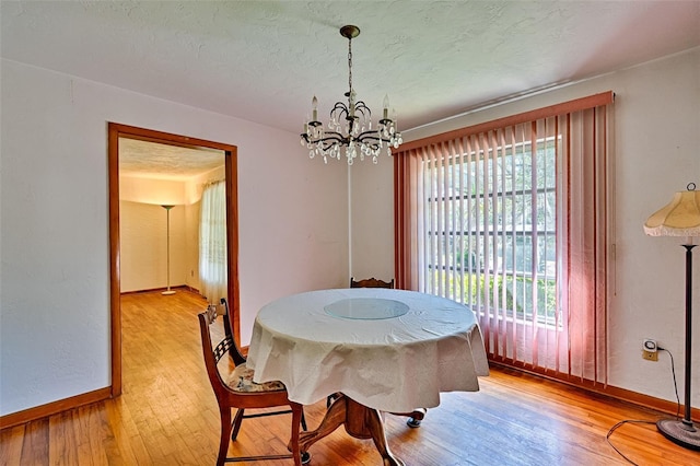 dining space with a chandelier, light wood-style flooring, a textured ceiling, and baseboards