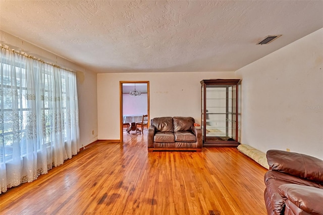 living area with a chandelier, visible vents, light wood finished floors, and a textured ceiling