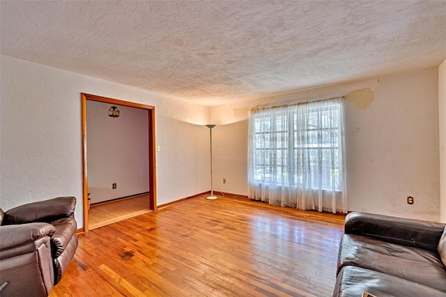 living room with baseboards, a textured ceiling, light wood-style flooring, and a textured wall