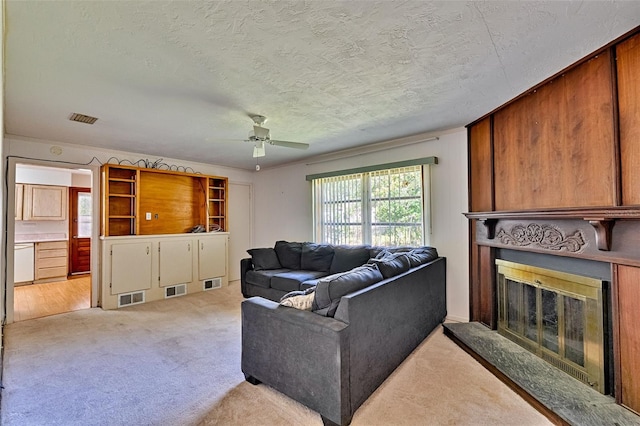 living room featuring visible vents, light carpet, a textured ceiling, and a glass covered fireplace