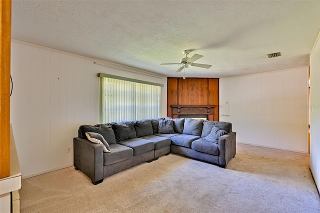 living area with visible vents, a ceiling fan, a textured ceiling, a fireplace, and light colored carpet