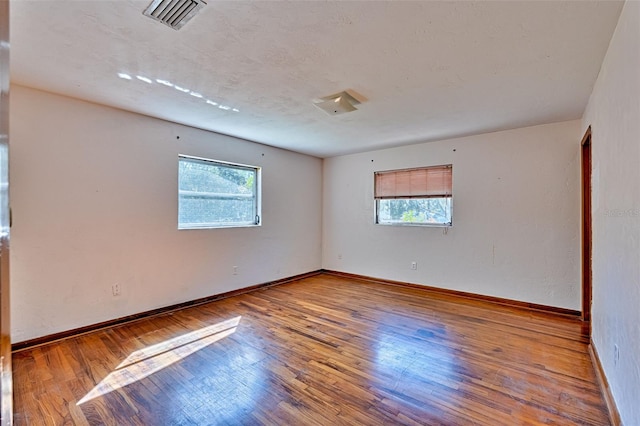 unfurnished room featuring hardwood / wood-style flooring, baseboards, visible vents, and a wealth of natural light