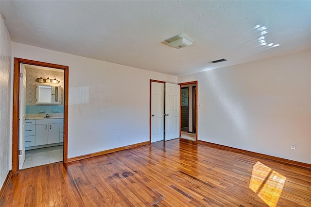 unfurnished bedroom with visible vents, wood-type flooring, baseboards, and ensuite bath