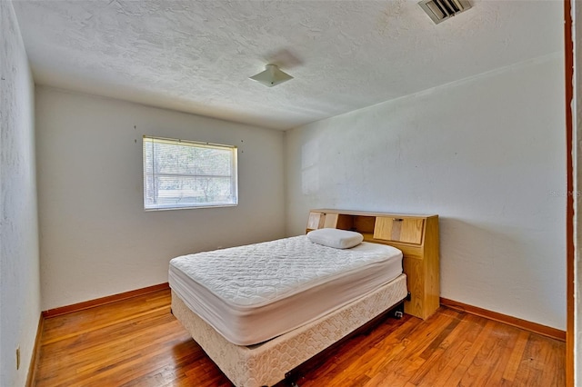 bedroom with visible vents, baseboards, light wood-style floors, and a textured ceiling