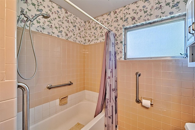 full bathroom featuring wallpapered walls, shower / bath combination with curtain, and a wainscoted wall