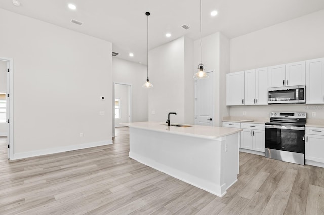 kitchen featuring visible vents, light wood-type flooring, appliances with stainless steel finishes, a towering ceiling, and a sink