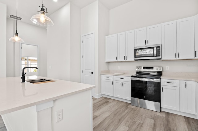 kitchen featuring light wood-style flooring, a sink, white cabinets, appliances with stainless steel finishes, and decorative light fixtures