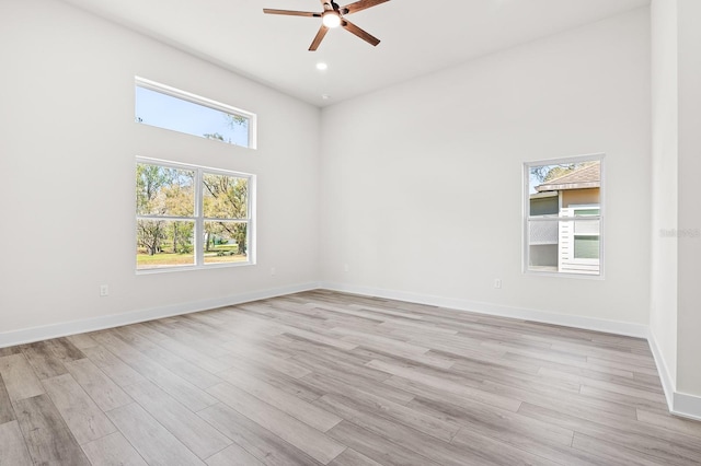 unfurnished room featuring a towering ceiling, light wood-style flooring, baseboards, and ceiling fan