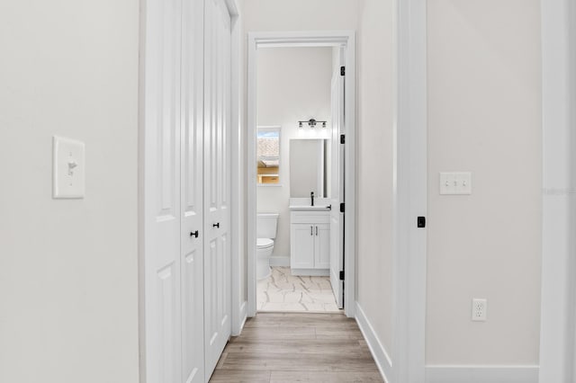 corridor featuring a sink, baseboards, and marble finish floor