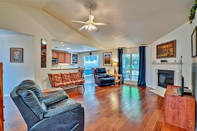 living area featuring a ceiling fan, wood finished floors, baseboards, lofted ceiling, and a fireplace with flush hearth