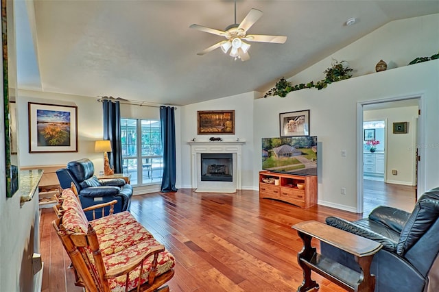 living room featuring a ceiling fan, wood finished floors, baseboards, a fireplace with flush hearth, and vaulted ceiling