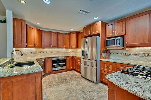 kitchen featuring a sink, light stone countertops, appliances with stainless steel finishes, and brown cabinets