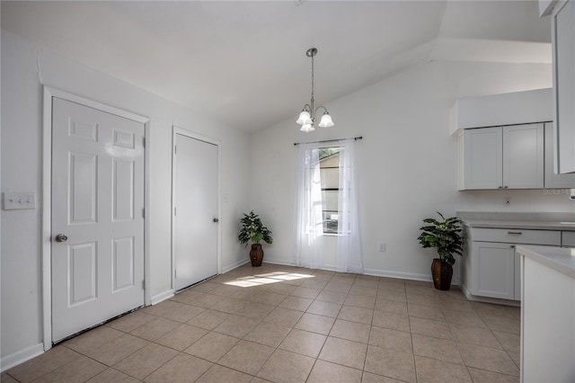 unfurnished dining area with lofted ceiling, light tile patterned floors, baseboards, and a chandelier